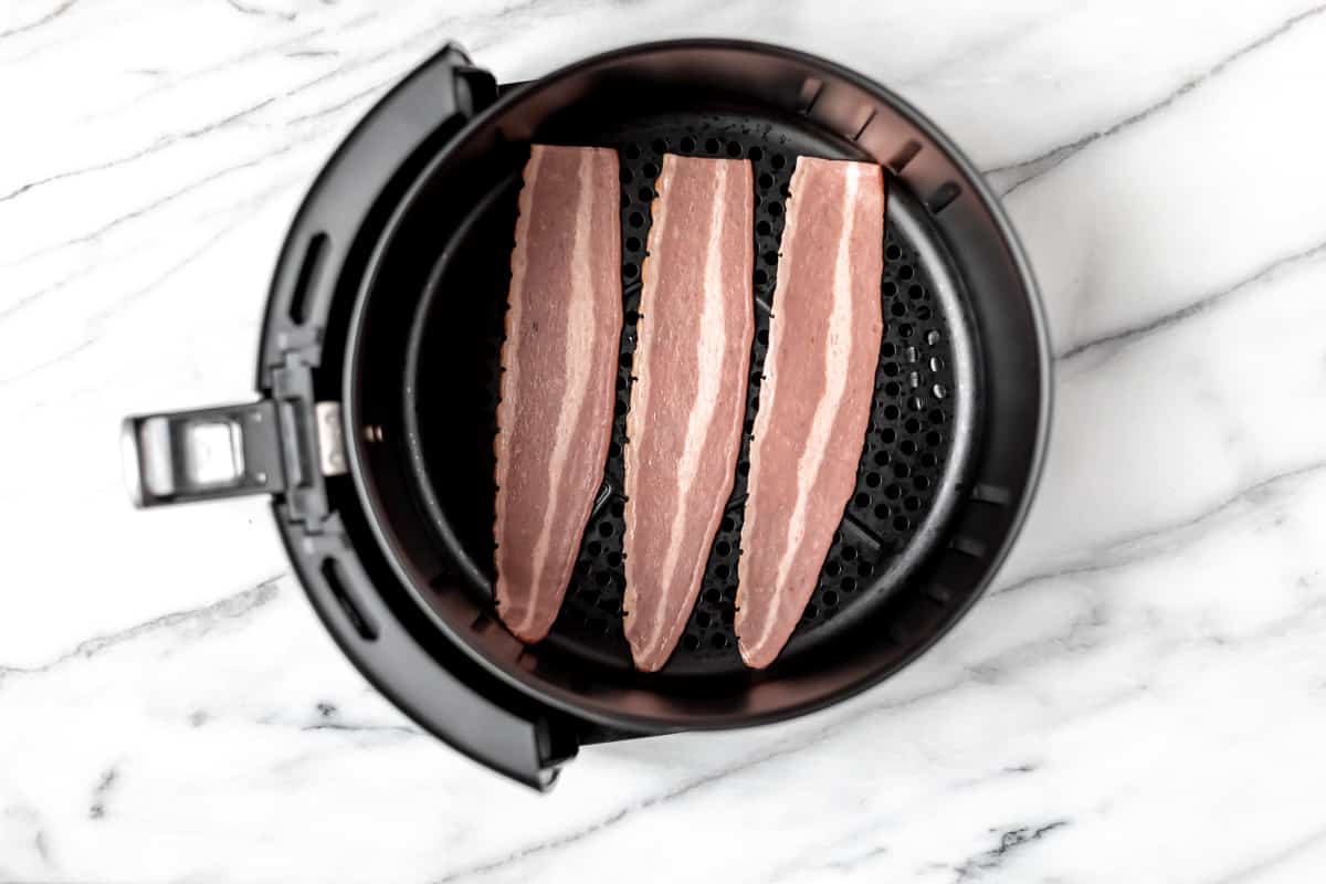 Three strips of turkey bacon in the basket of an air fryer.