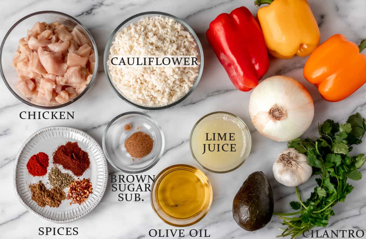 Ingredients needed to make chicken fajita bowls over cauliflower rice on a marble background with text overlay.