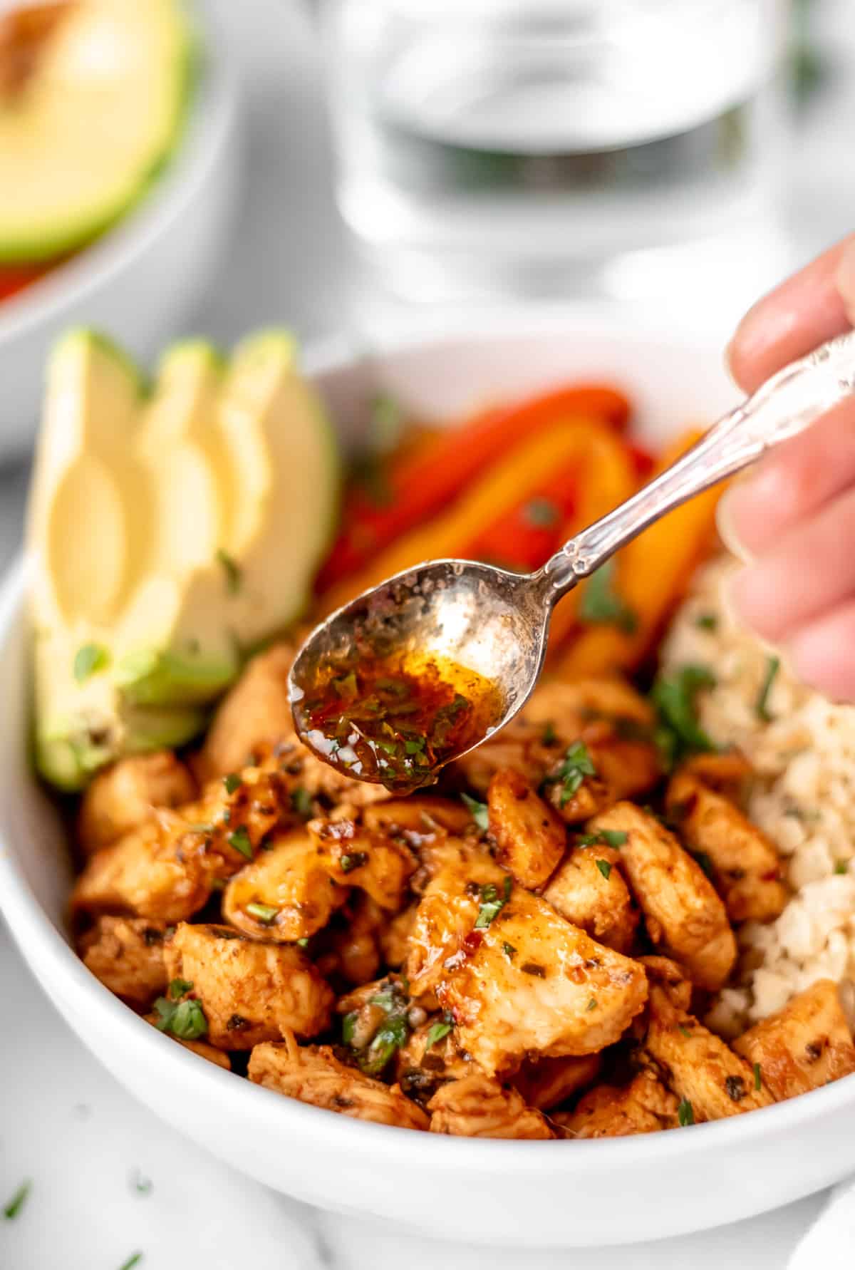 Fajita sauce being drizzled over a chicken fajita bowl with chunks of chicken, avocado, peppers and cauliflower rice in it.