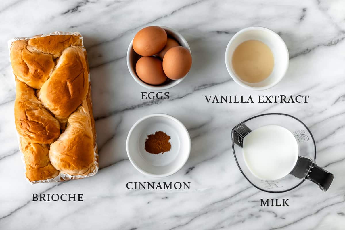 Ingredients needed to make french toast on a marble background with text overlay.