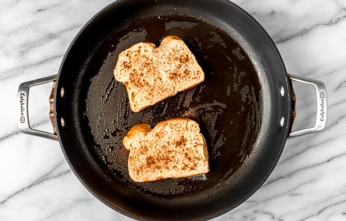Two slices of uncooked French toast in a black skillet.