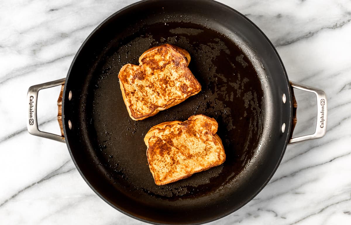 Two slices of cooked French toast in a black skillet.
