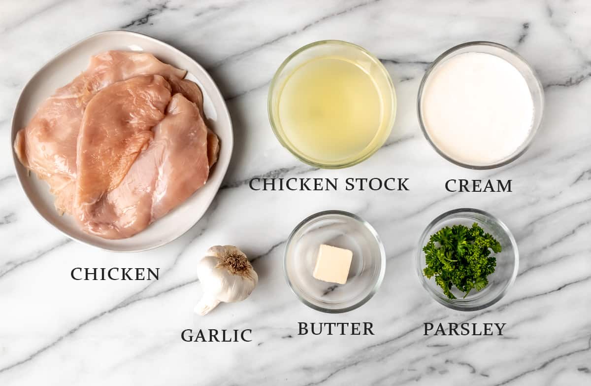 Ingredients needed to make creamy garlic chicken on a marble background with labels.