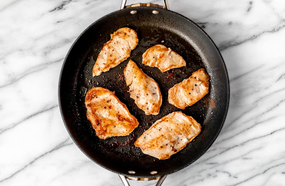 Six pieces of seared chicken in a black skillet.