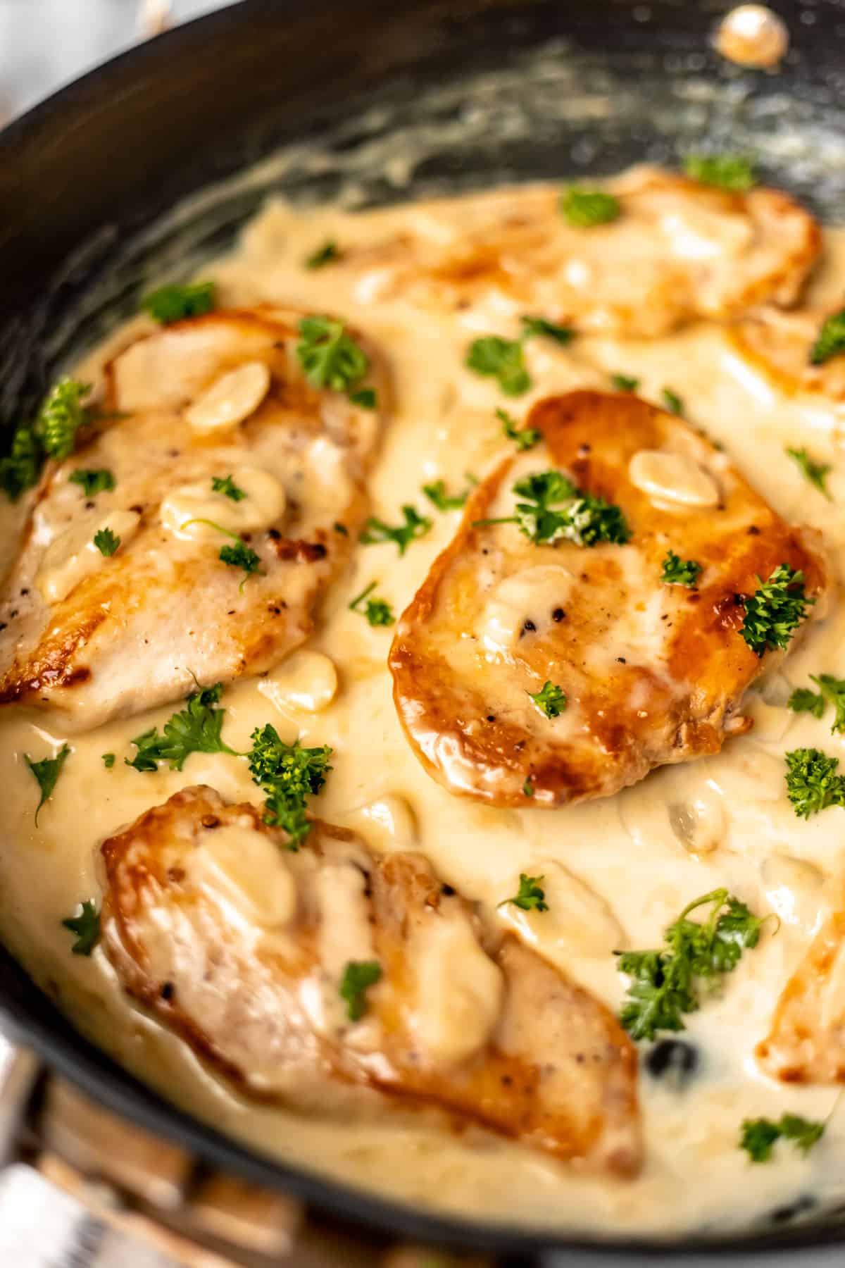 Close up of creamy garlic chicken garnished with parsley in a black skillet.