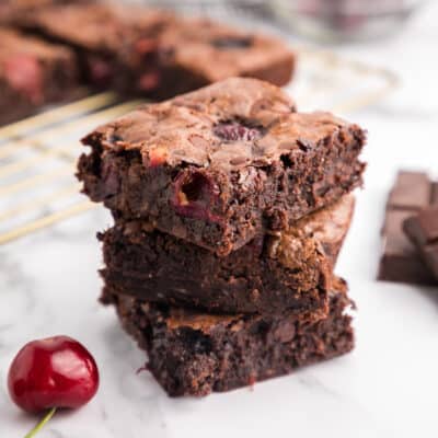 A stack of three double chocolate cherry brownies with a cherry and more brownies in the background.