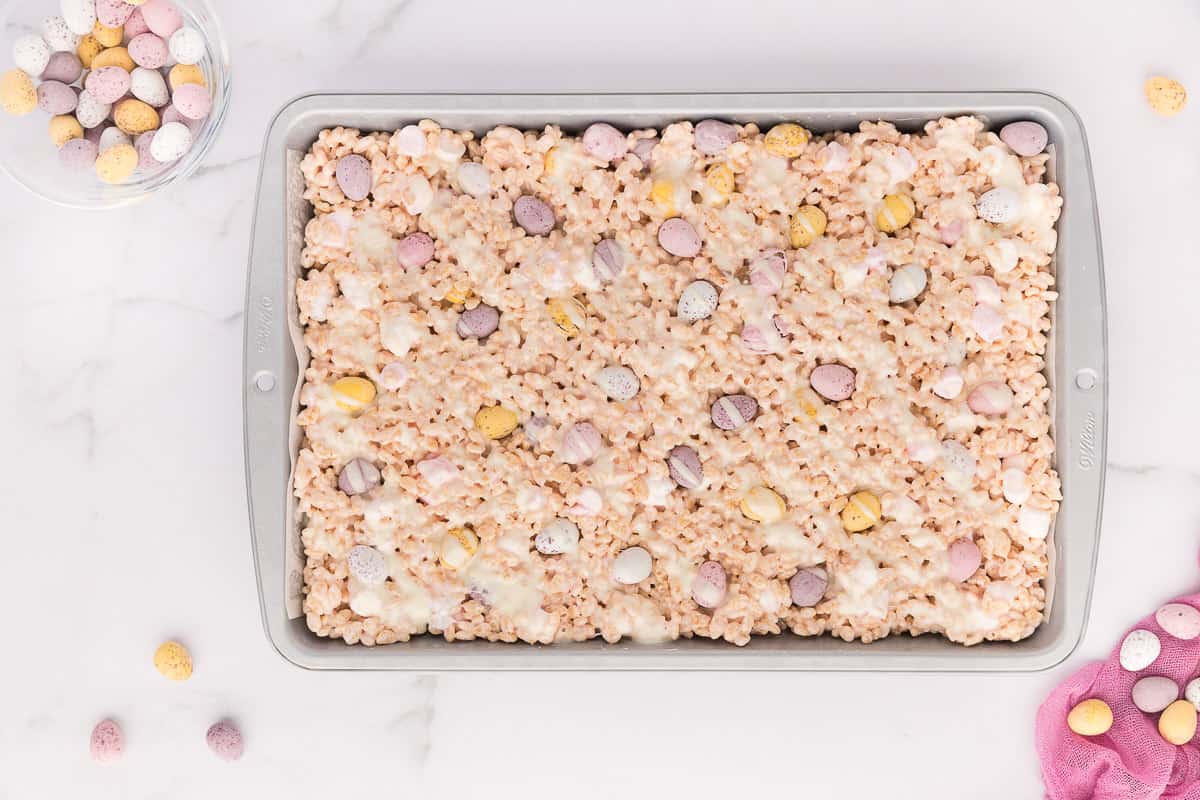 Easter Rice Krispie Treats decorated with mini candy eggs and white chocolate drizzle in a rectangular baking pan.