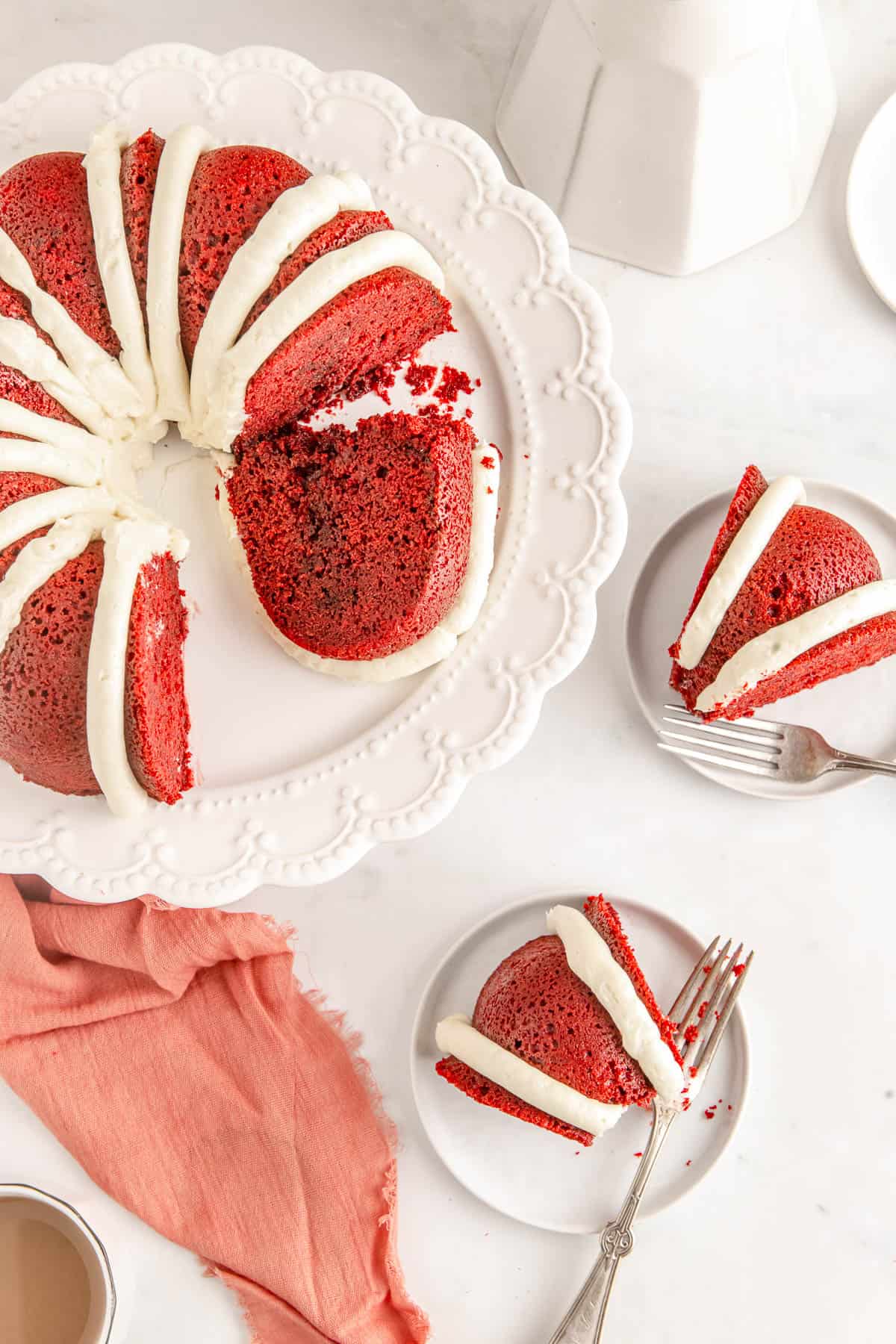Overhead of a red velvet pound cake on a cake stand with two servings of red velvet cake on white plates.