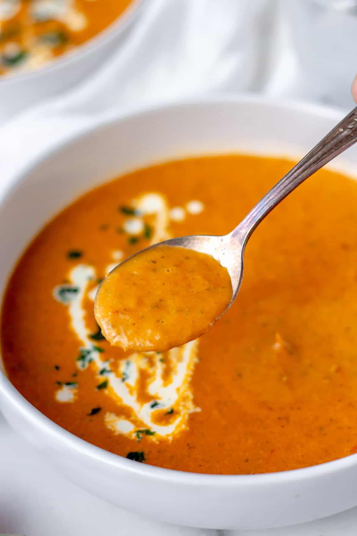 A spoonful of roasted tomato soup being lifted up over a bowl of soup.