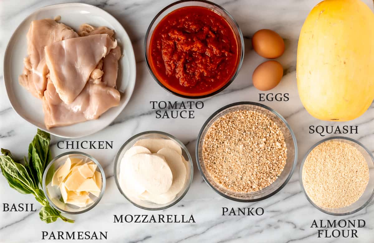 Ingredients needed to make spaghetti squash chicken parmesan on a marble background with text overlay.