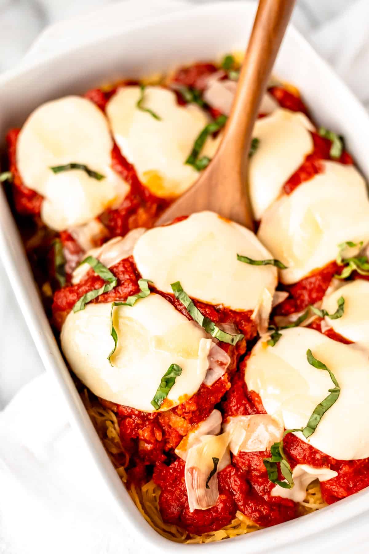 A wood turner lifting up a piece of chicken in a chicken parmesan casserole.