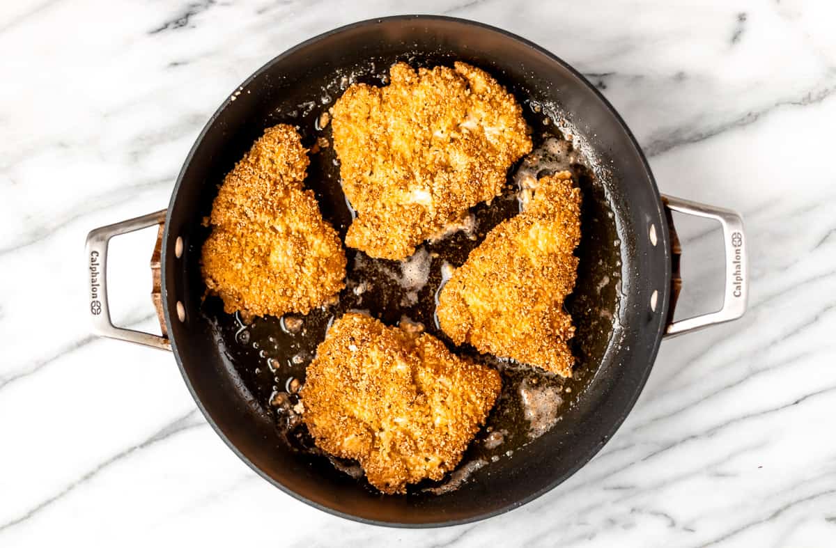 Four pieces of fried chicken in a black skillet.