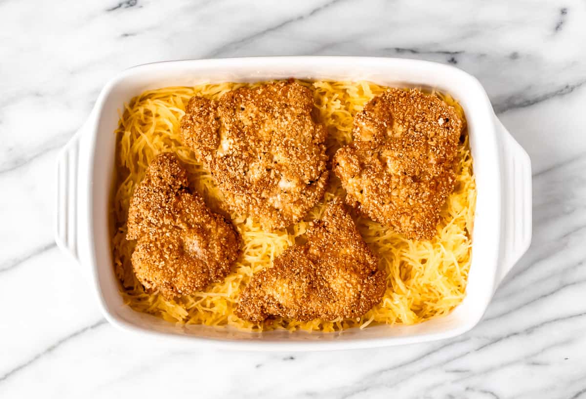 Four pieces of fried chicken on top of spaghetti squash in a casserole dish.
