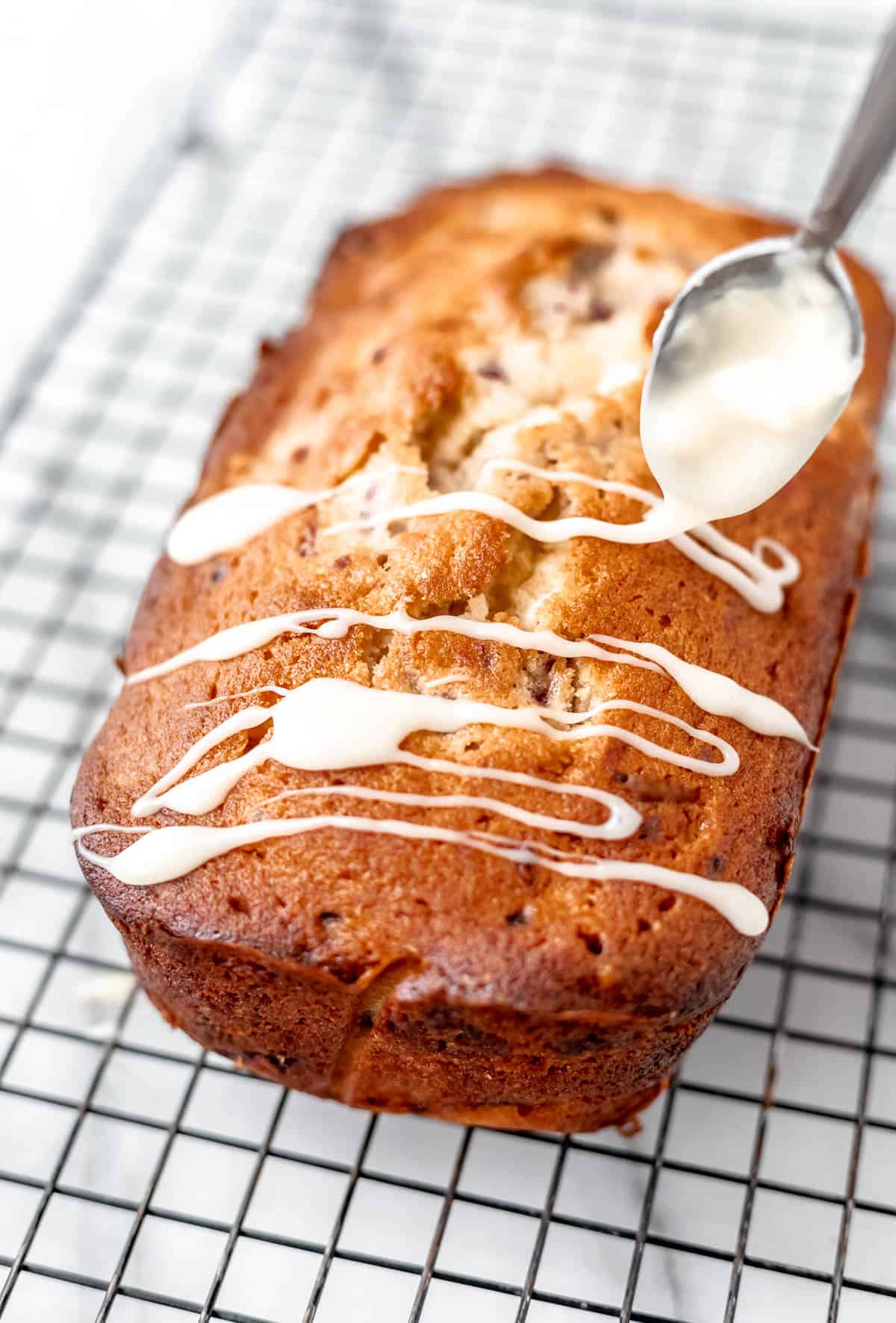 White chocolate being drizzled over a loaf cake on a cooling rack.
