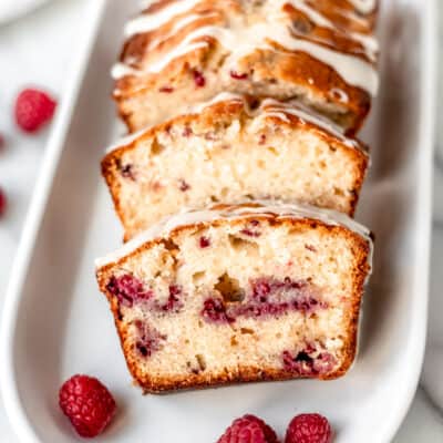 Slices of white chocolate raspberry loaf cake on a serving tray with raspberries.