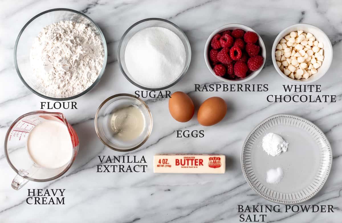 Ingredients needed to make a white chocolate raspberry loaf cake on a marble background with text overlay.
