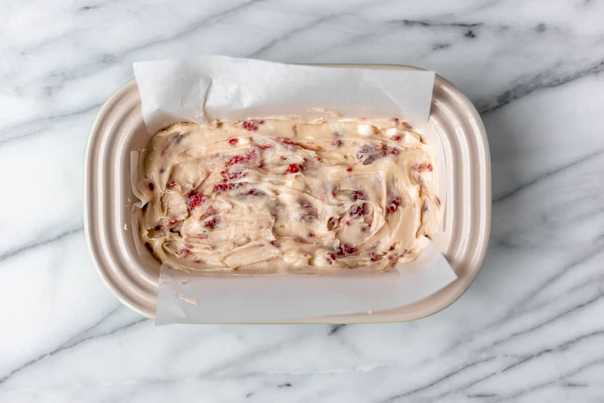 A loaf pan with white chocolate raspberry cake batter in it.