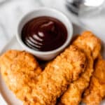 Air fryer chicken tenders with barbecue sauce in a white bowl on a white plate.