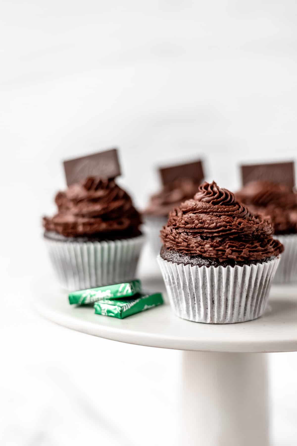 A cake stand with Chocolate Mint Cupcakes and Andes candies on it.