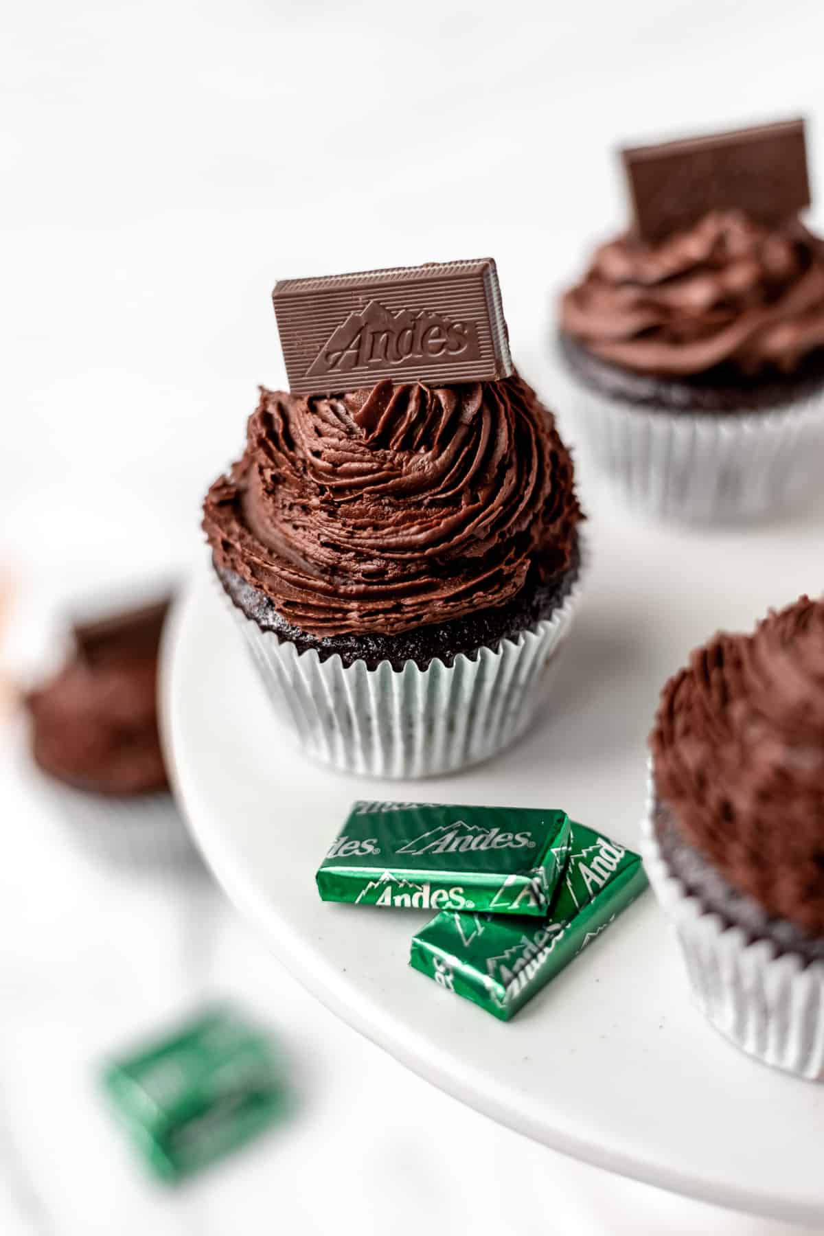 A cake stand with Chocolate Mint Cupcakes and Andes candies on it.