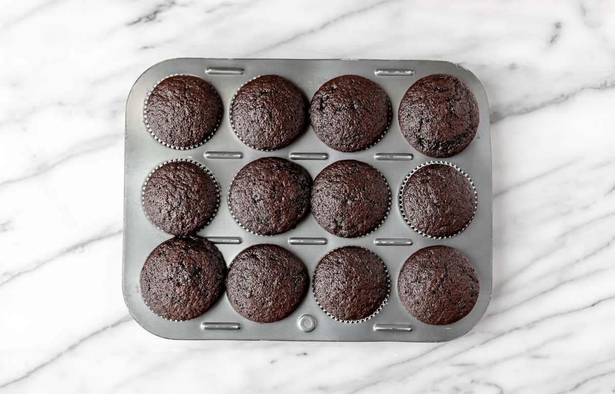 Twelve baking chocolate mint cupcakes in a cupcake pan.