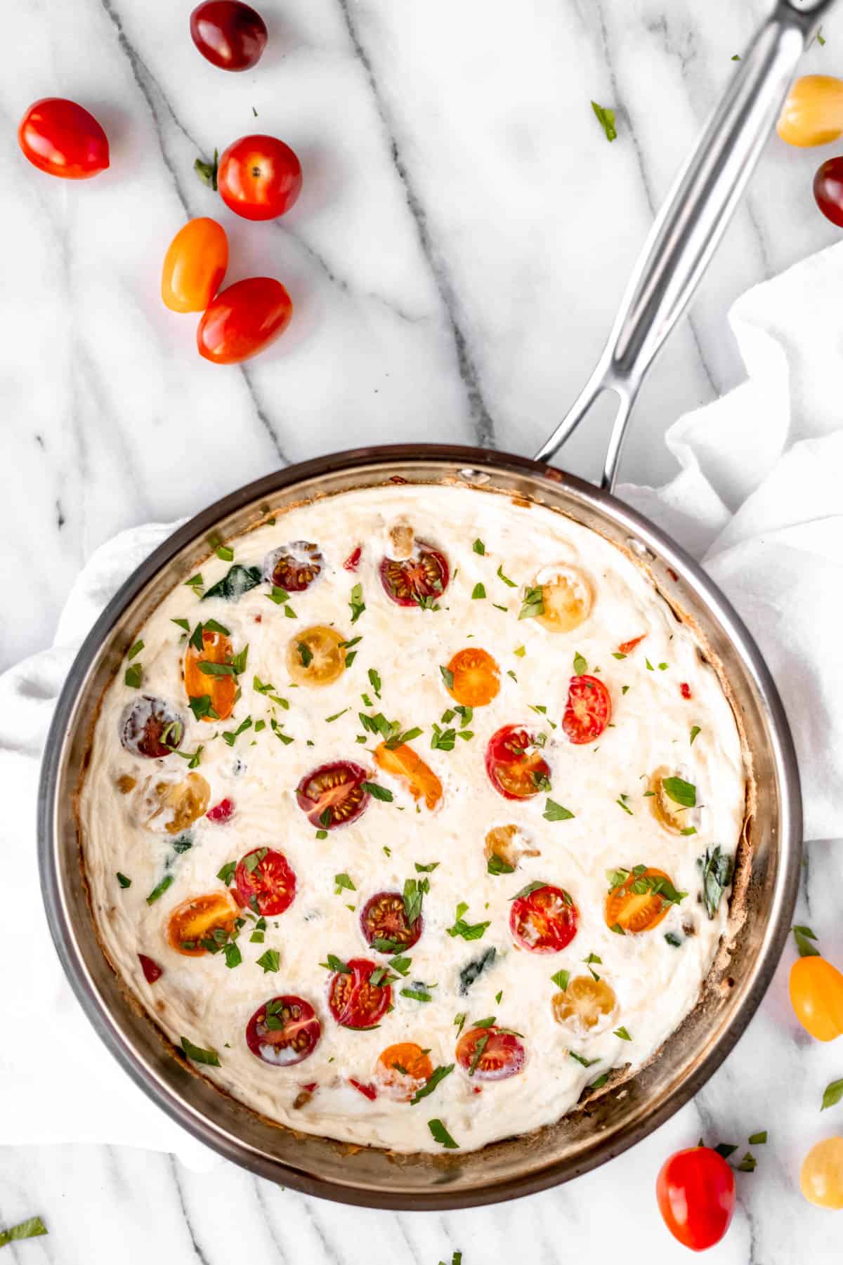 Overhead of an egg white frittata with vegetables in a silver skillet with multi-colored cherry tomatoes scattered around it.