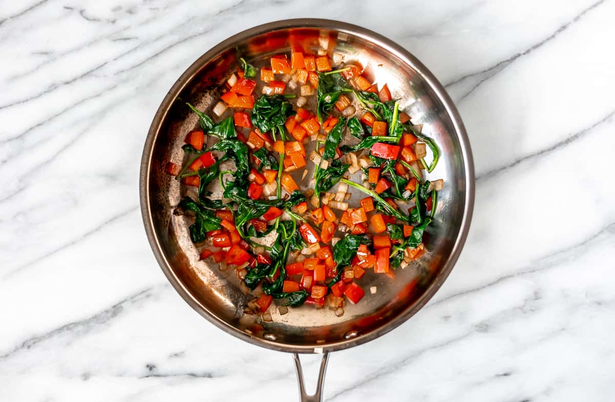 Red peppers, spinach and shallots cooking in a silver skillet.