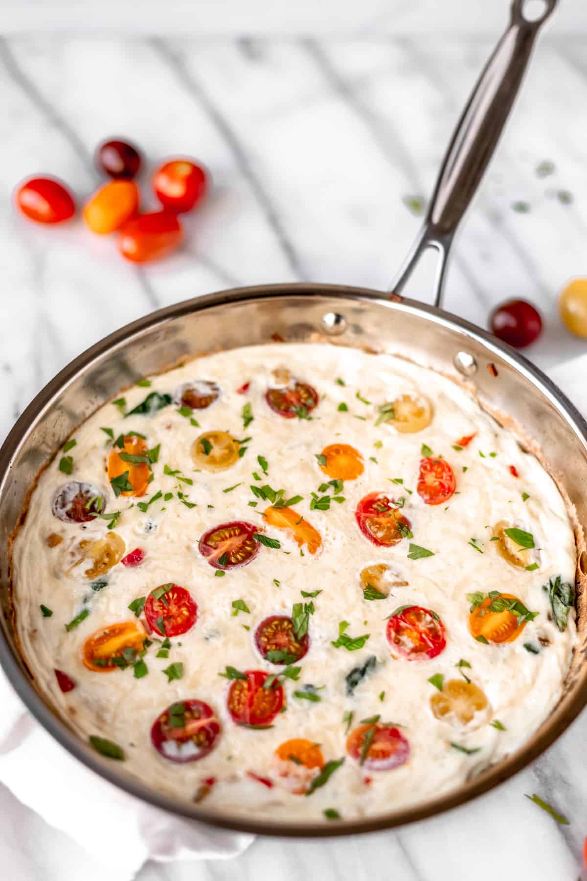 An egg white frittata with vegetables in a silver skillet with red, orange, purple and yellow tomatoes around it.