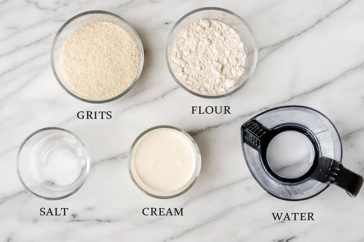 Ingredients needed to make fried grits cakes in bowls on a marble background with text overlay.