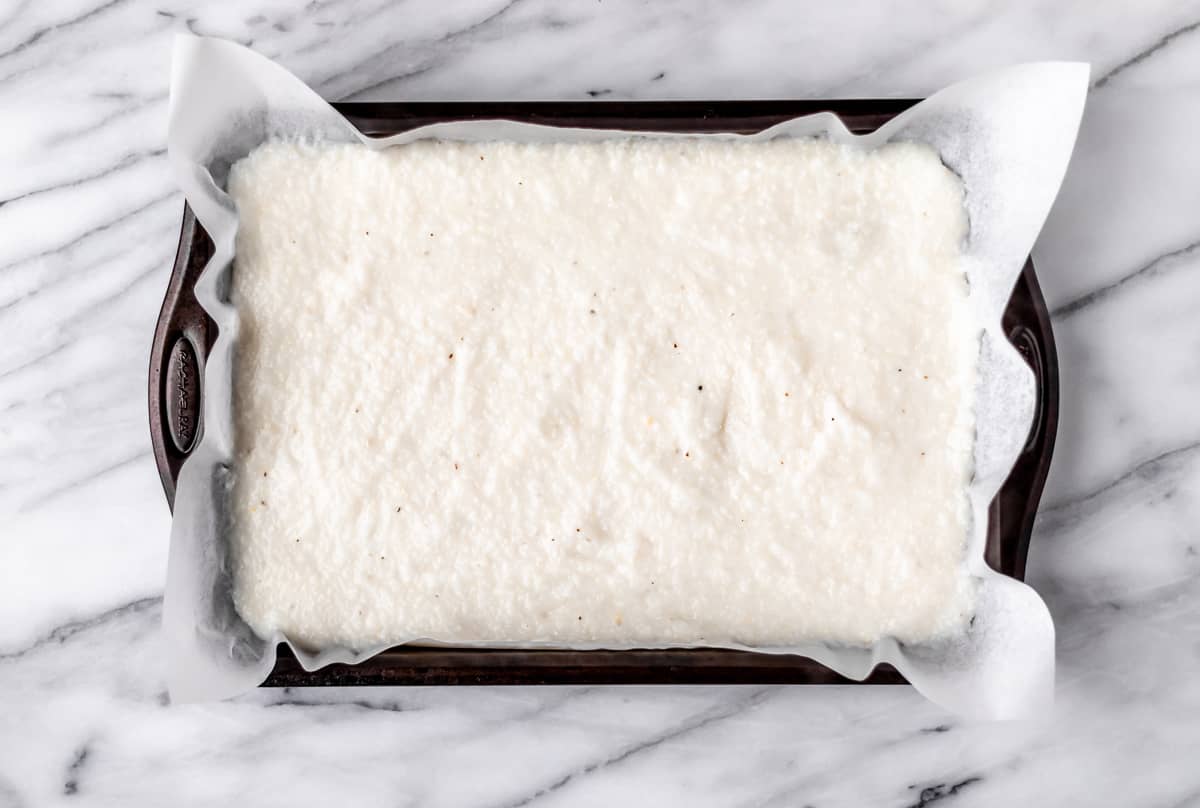Prepared grits spread out on a parchment paper lined baking sheet.a