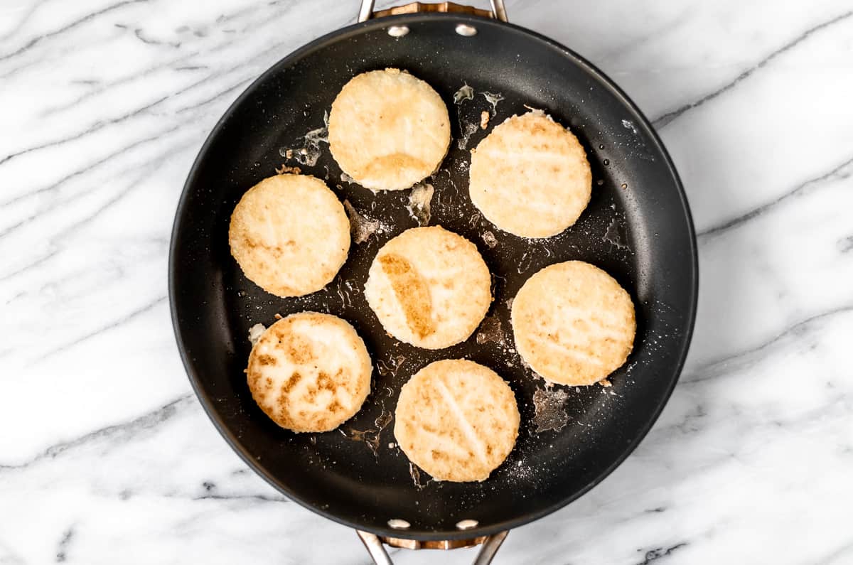 Fried grits cakes in a black skillet over a marble background.
