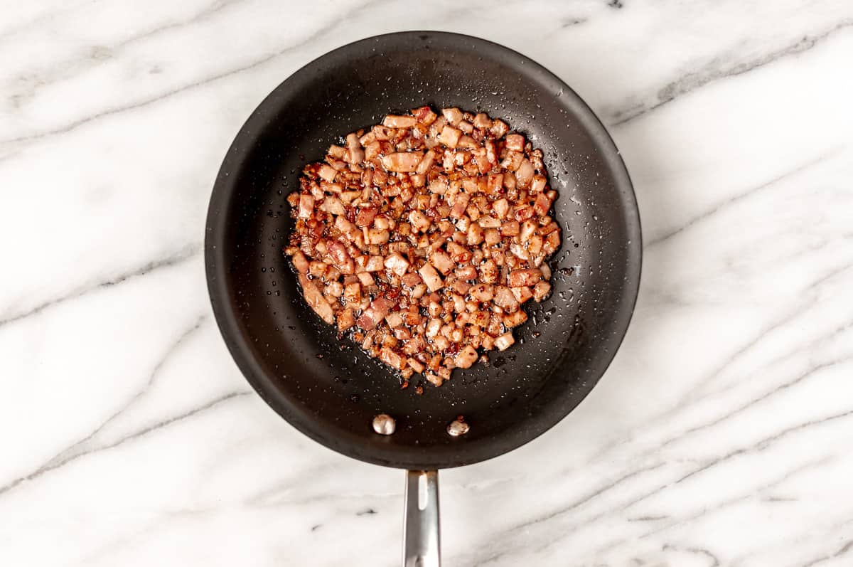 Diced ham cooked in a small black skillet over a marble background.