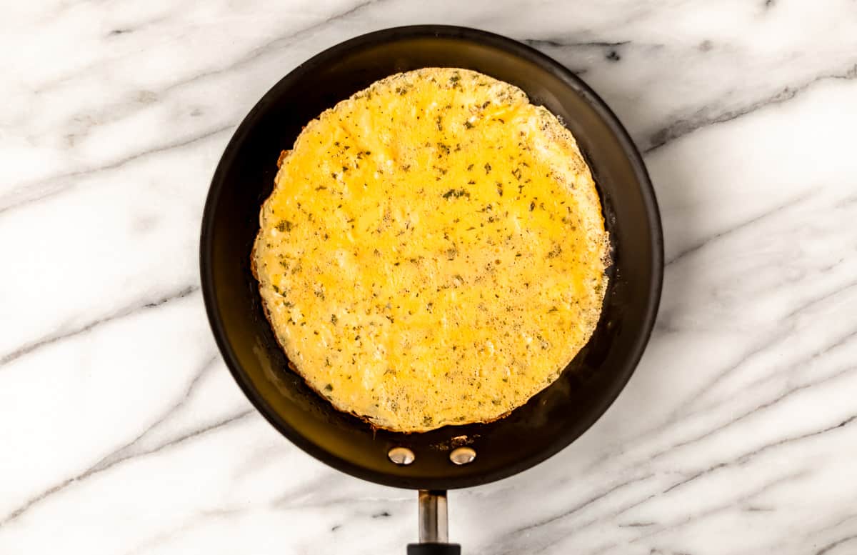 An egg omelet without filling on it yet in a black skillet over a marble background.