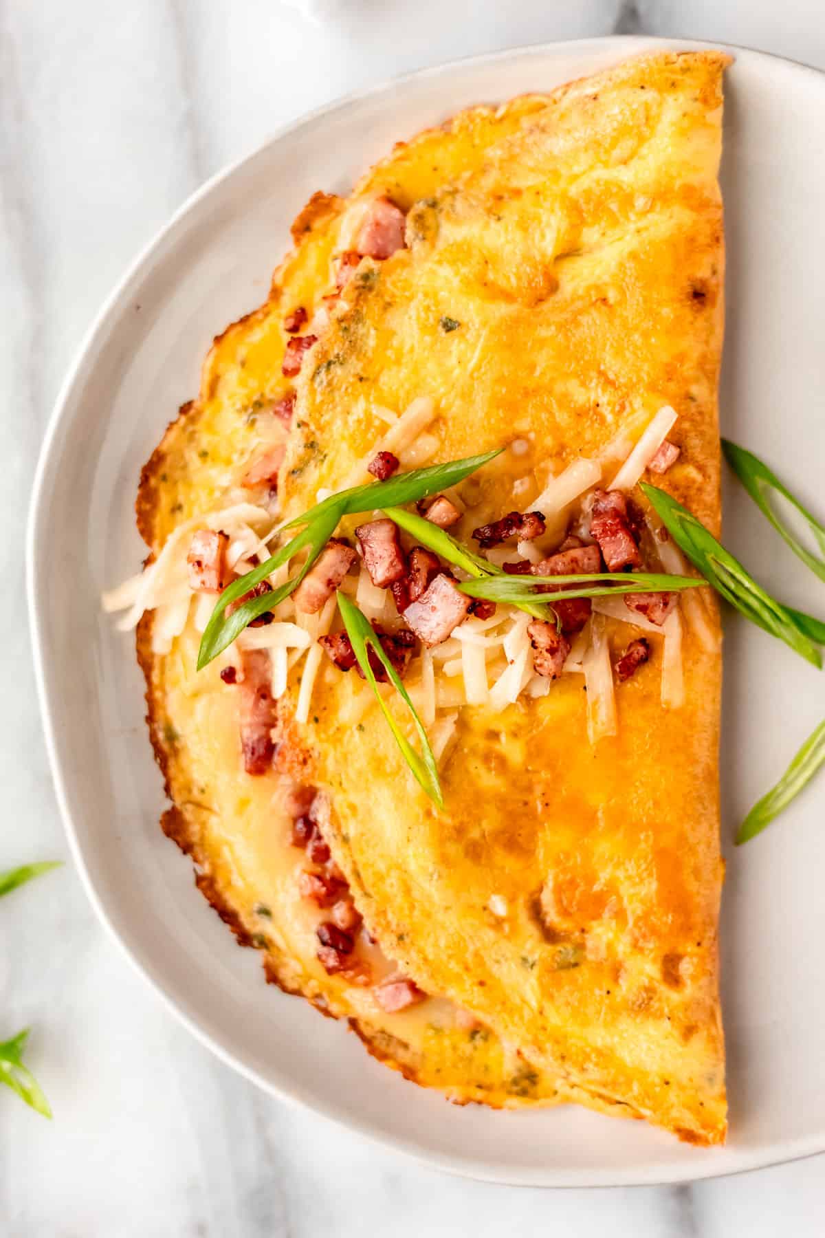 Close up of a ham and cheese omelet garnished with diced ham, cheese and green onions.