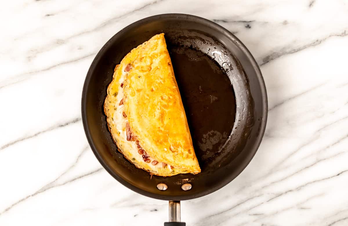 Am omelet folded in half in a black skillet over a marble background.