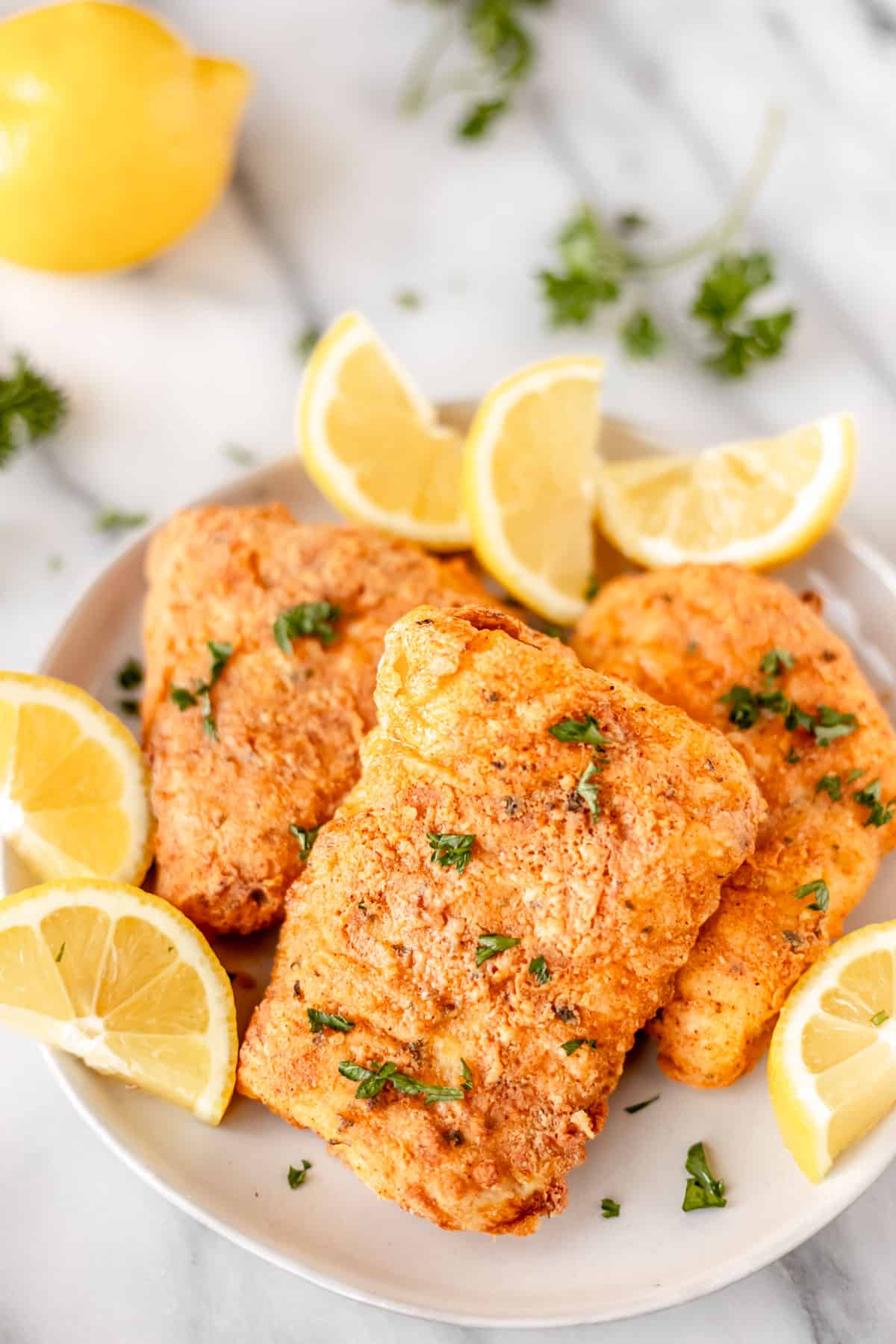 A plate of air fryer cod with fresh parsley and lemon slices for garnish.