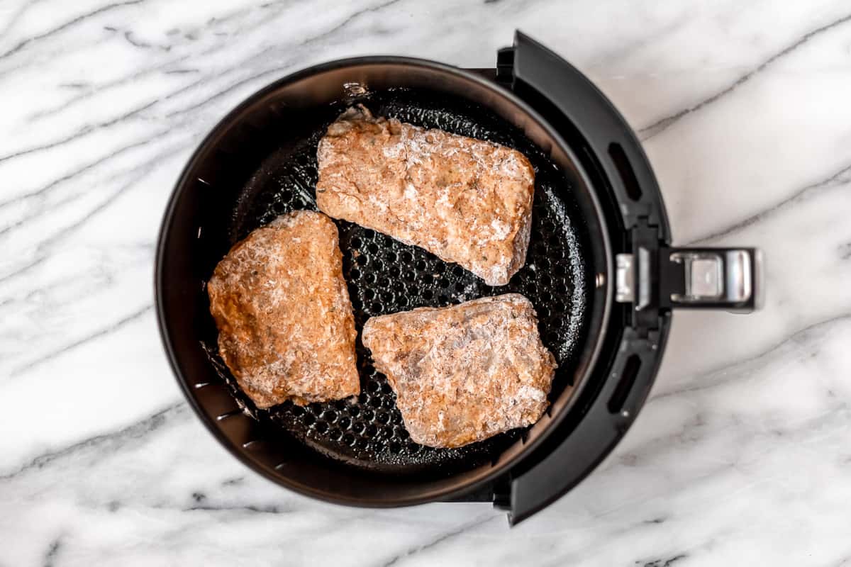 Uncooked breaded cod fillets in the basket of an air fryer.