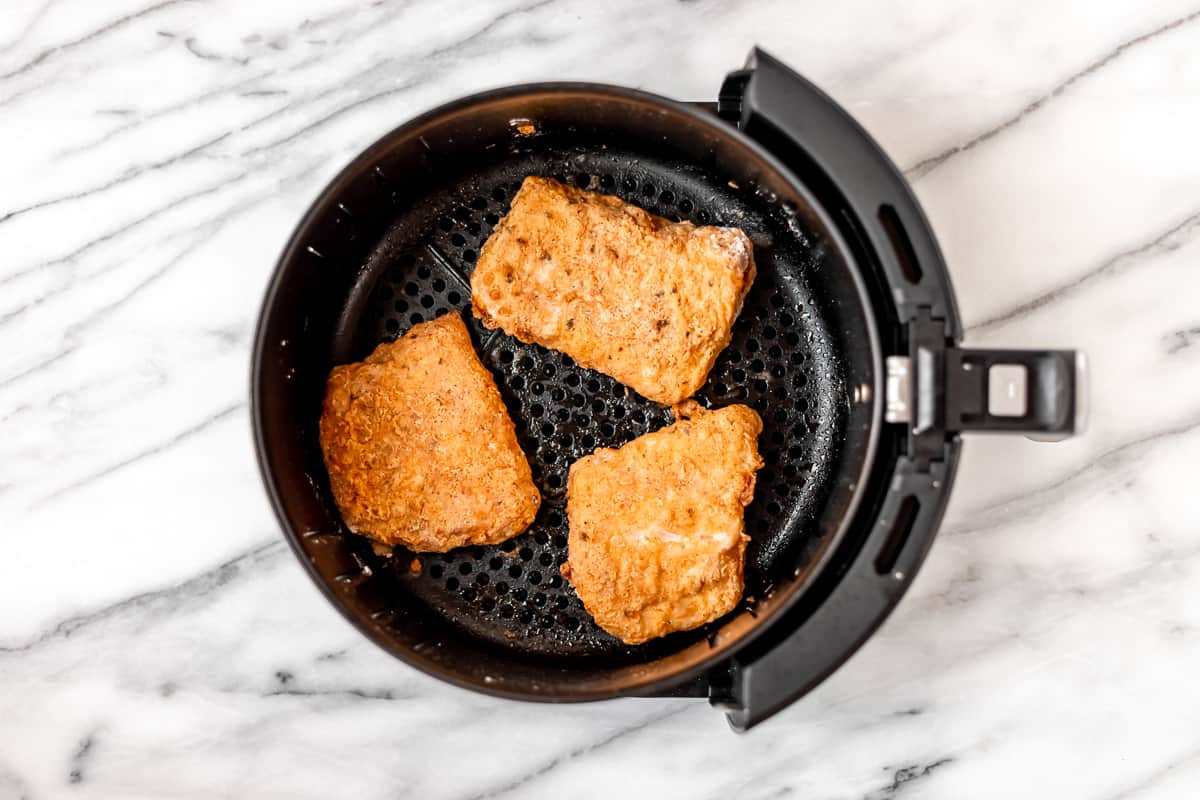 Cooked cod fillets in the basket of an air fryer.