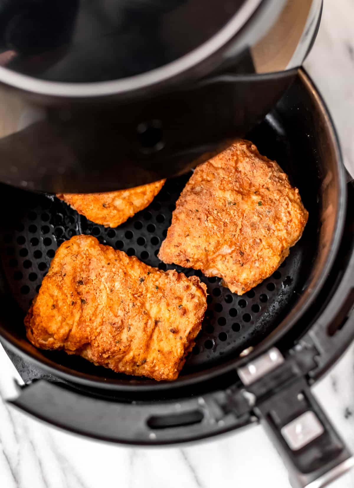 Cooked breaded cod fillets in the a partially pulled out drawer of an air fryer.