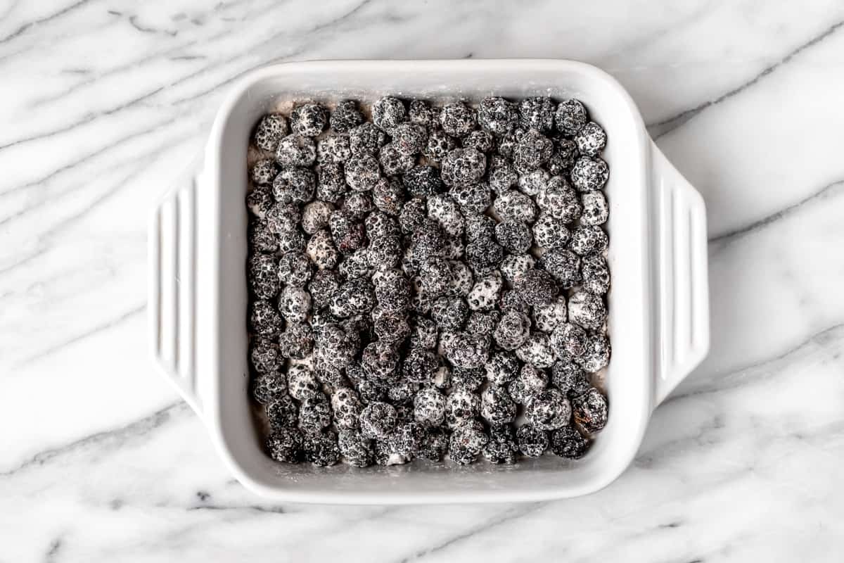 Blackberries coated in flour and sugar in a white, square baking dish.