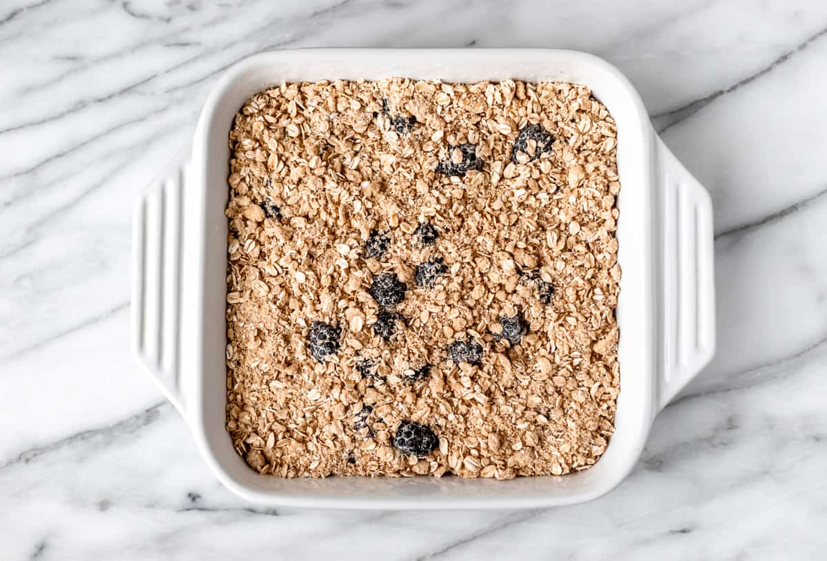 Unbaked blackberry crisp topped with an oat crumble in a white, square baking dish.