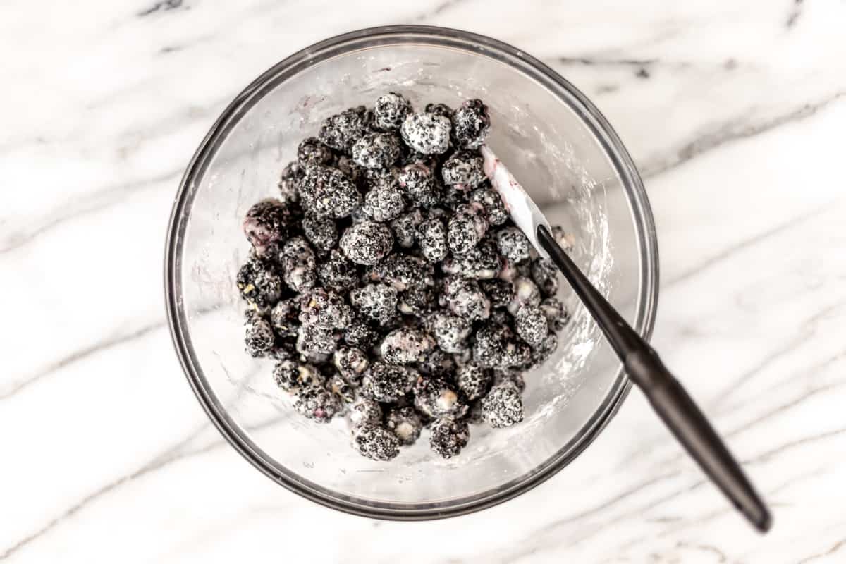 A bowl of blackberries tossed in sugar and cornstarch with a spatula in it.
