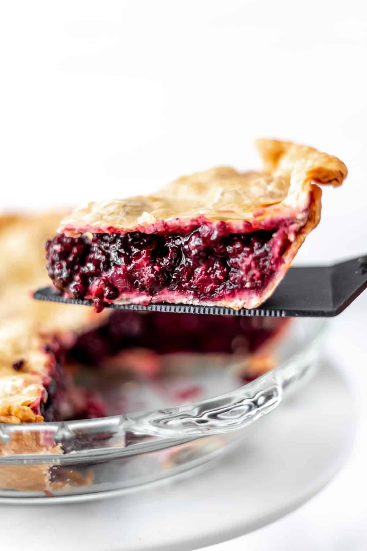 A slice of blackberry pie being lifted up over the pie plate.