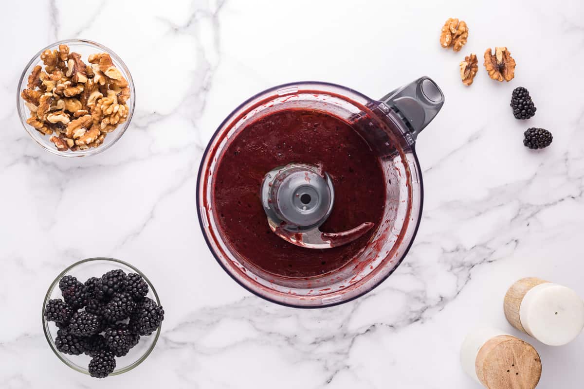 Blackberry salad dressing in a food processor bowl with small bowls of ingredients around it.