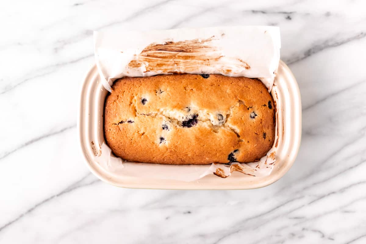 A baked blueberry lemon pound cake in a loaf pan on a marble background.