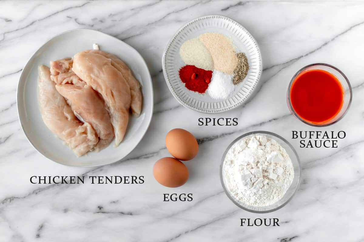 Ingredients needed to make buffalo chicken tenders on a marble background with text overlay.