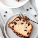 A slice of chocolate chip pound cake on a white plate with the serving tray of. more slices near it and text overlay.