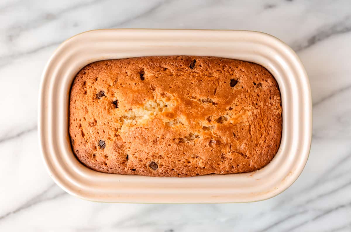 A baked chocolate chip pound cake in a loaf pan over a marble background.