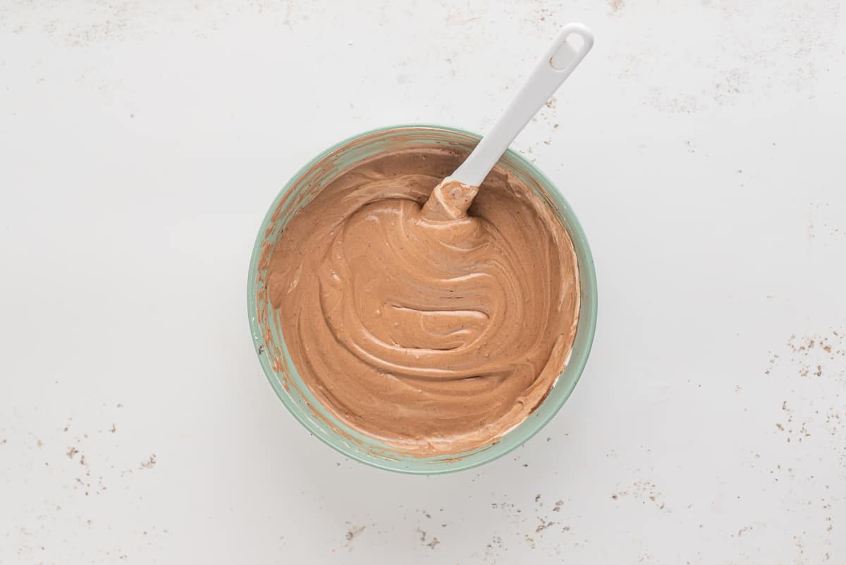 Chocolate pudding and whipped cream blended together in a bowl with a whisk.