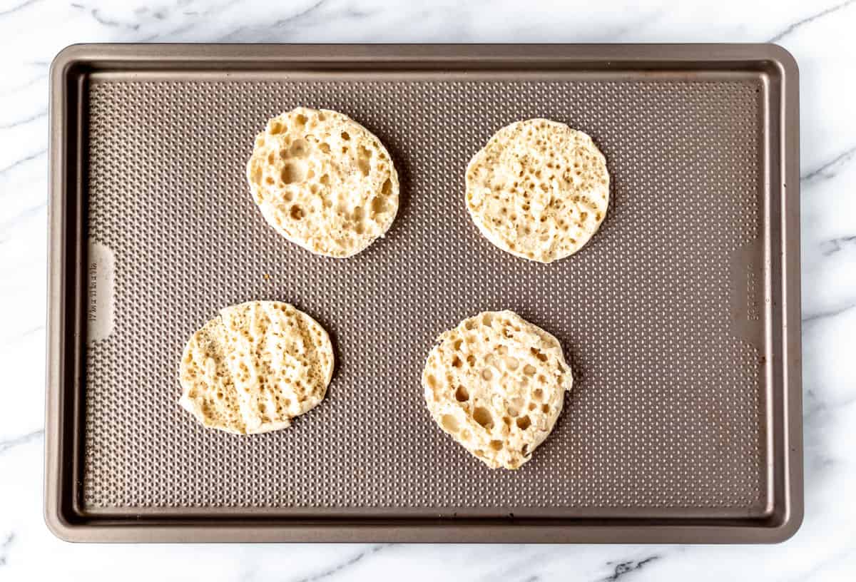 Four English muffin halves on a baking sheet.